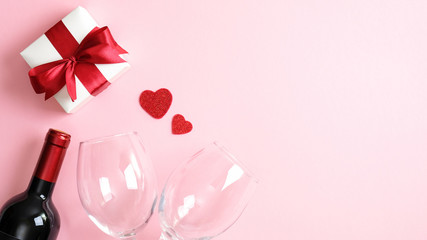 Valentines day greeting cart template. Flat lay white gift box with red ribbon bow, bottle of wine champagne, two glasses and hearts on pink background. Happy Valentines day, romantic dinner concept