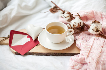 Obraz na płótnie Canvas Beautiful white cup with tea on the bed, pink knitted plaid, postcard Happy Valentine's Day. Breakfast in bed. Morning. Spring. Cozy.