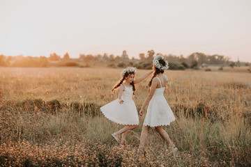 Happy mother and daughter in white dresses are spinning and have joy and happiness in summer