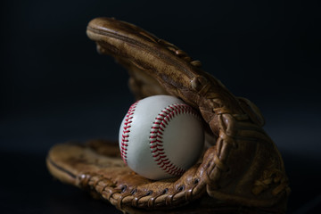 Baseball in a glove on black background.