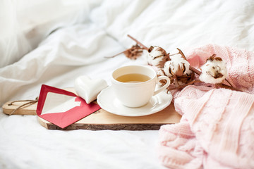 Beautiful white cup with tea on the bed, pink knitted plaid, postcard Happy Valentine's Day. Breakfast in bed. Morning. Spring. Cozy.