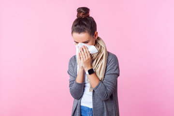 Flu season. Portrait of sick brunette teenage girl with bun hairstyle wearing pullover and scarf,...