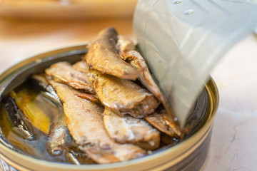 Female hands open a can of fish sprats on the table close up