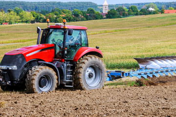 Farmer in red tractor preparing land with plow for sowing