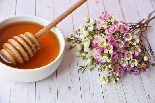 Pink and white manuka flower and honey in a white bowl and dipper in it