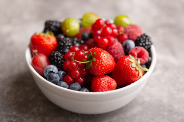 Bowl with fresh summer berries on a gray background.