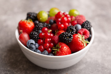 Bowl with fresh summer berries on a gray background.