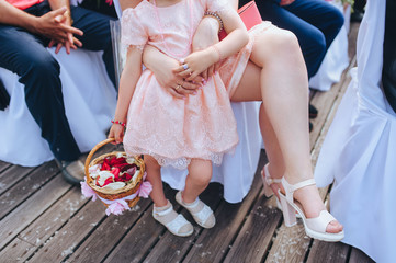 Little child girl in a beige dress with a basket with flower petals at the ceremony. Photography,...