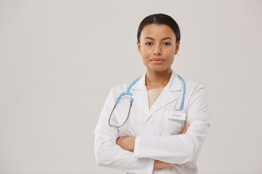 Waist up portrait of beautiful African-American nurse posing confidently while standing with arms crossed against white background, copy space