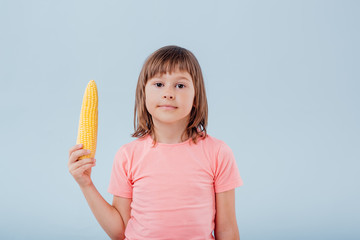  little girl has a corn in her hand. isolated on blue background, copy space, in studio, profile view - obrazy, fototapety, plakaty