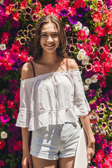 young beautiful girl on a background of bright flowers of a petunia with a skateboard in hand