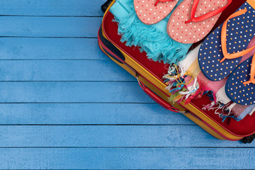 Suitcase with flip-flops and beach towels on wooden table.