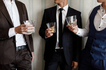 stylish friends businessmen in suits toasting with glasses of whiskey indoors, closeup. groom's morning