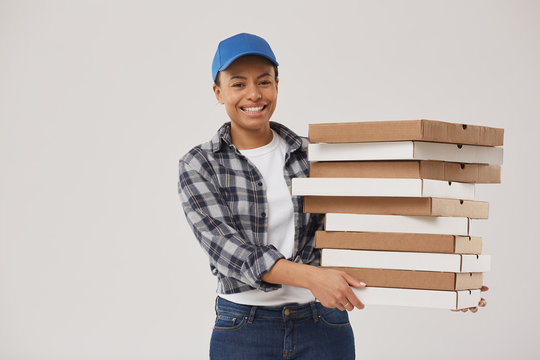 Waist up portrait of beautiful mixed race young woman holding pizza boxes and smiling at camera while working for fast food delivery and posing against white background, copy space