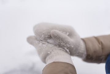 Woman makes a snowball in the hands of white mittens