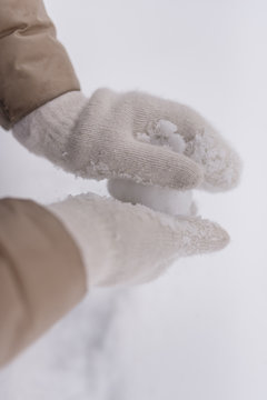 Woman makes a snowball in the hands of white mittens