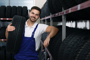 Male mechanic with car tire in auto store