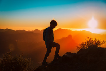 Silhouettes of young boy hiking at sunset mountains