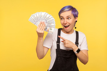 Portrait of surprised stylish hipster girl with violet short hair in denim overalls pointing at fan...