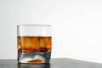 Glass of aged golden whiskey with ice cubes on the table. Amber colored alcohol beverage with rocks at the bar