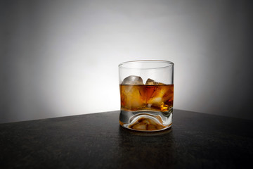 Glass of aged golden whiskey with ice cubes on the table. Amber colored alcohol beverage with rocks at the bar
