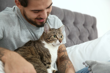 Happy man with cat on bed at home. Friendly pet