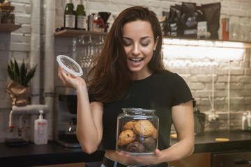 young beautiful woman barista enjoying nice aroma while opening jar with cookies