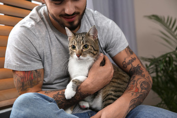 Man with tabby cat near window indoors, closeup. Friendly pet