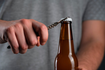 Men opening cold bottle of beer with cap on black background. Hands cracking refrigerated wheat or...