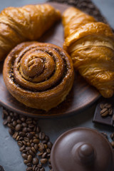 Croissants and a bun are lying on a large plate; next to them is a lid for pigs on a table