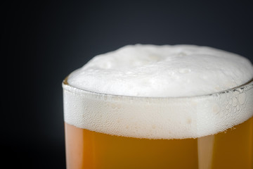 Fresh and cold glass craft beer with white foam on top on black background with space for text. Foamy wheat or lager beer on dark background