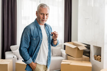mature man holding keys and looking at camera in new house