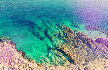 Top view of blue sea water and stone shore or rocky coast. Ocean waves landscape background, instagram toned style. Natural texture background
