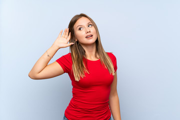 Teenager girl over isolated blue background listening something