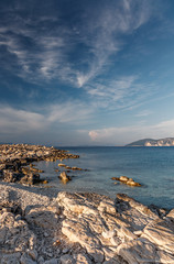 Fototapeta na wymiar Fantastic rocky beach coastline during sunset. impressively beautiful seascape with picturesque sky over calm blue ocean under warm sunlight at sunrise. Picturesque evening and gorgeous scene. Greece