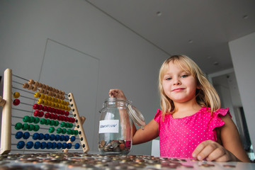 cute girl saving money for education, child put coins into jar