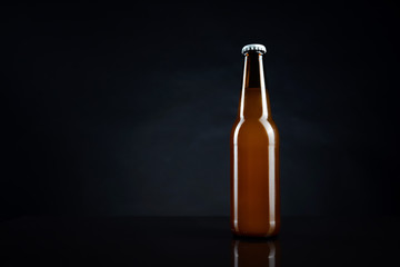 Cold unopened bottle of beer with cap on black background. Glass of refrigerated wheat or lager beer on dark background