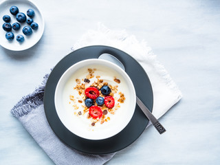 Joghurt mit frischen Himbeeren, Heidelbeeren und Müsli in einer weißen Schüssel mit Stoffserviette, servierfertig, Draufsicht