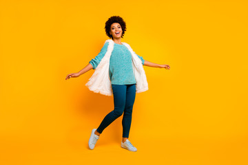 Full body photo of cheerful funky afro american girl relax rest fun on autumn holidays enjoy rejoice emotions wear shine turquoise sweater outfit isolated over yellow color background