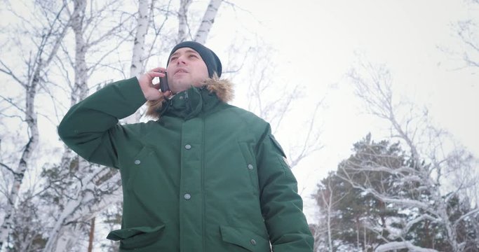 A man in winter in forest dialing a phone number and smiling. Talking