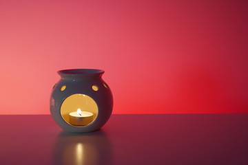 Aroma lamp with burning candle, reflection, red background. Relax, spa, healthcare concept. Close-up, copy space
