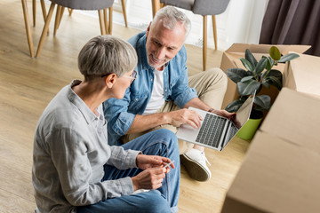 Fototapeta premium high angle view of mature man with laptop talking with woman in new house