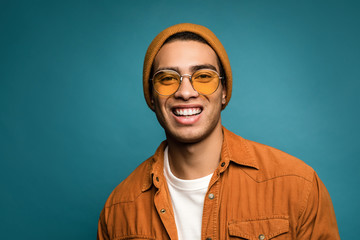 Photo of attractive amused mixed race man in yellow outfit, wearing hat and glasses smiling in good...