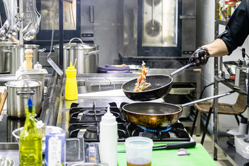 Chef in the kitchen at the restaurant prepares dishes,holds a frying pan in his hands and throws it upwards with fire