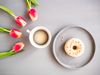 Fototapeta na wymiar Frische Tulpen, eine Tasse Kaffee und ein Donat mit Herzen auf einem grauen Hintergrund, Frühling, Flat la