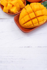 Fresh mango,beautiful chopped fruit with green leaves on bright wooden table background. Tropical fruit design concept, close up, copy space.