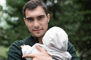 brunette dad with baby in his arms in the Park