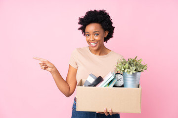 African american woman making a move while picking up a box full of things surprised and pointing...