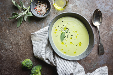 Green Broccoli cream soup in a gray bowl on stone background, top view