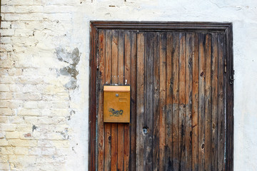 Old fashioned wooden door, yellow rusty postbox and white brick and concrete wall background
